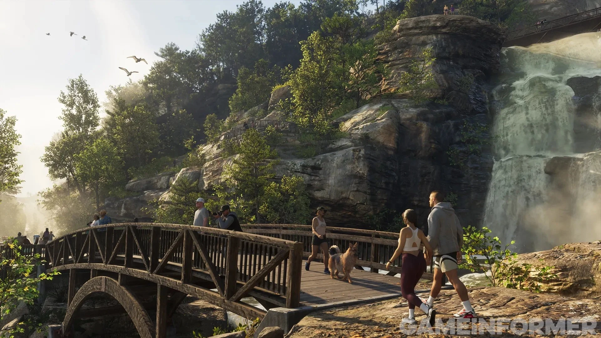 Capture de GTA VI publiée par Game Informer : un couple de randonneurs traverse une passerelle en bois devant une cascade, dans une forêt