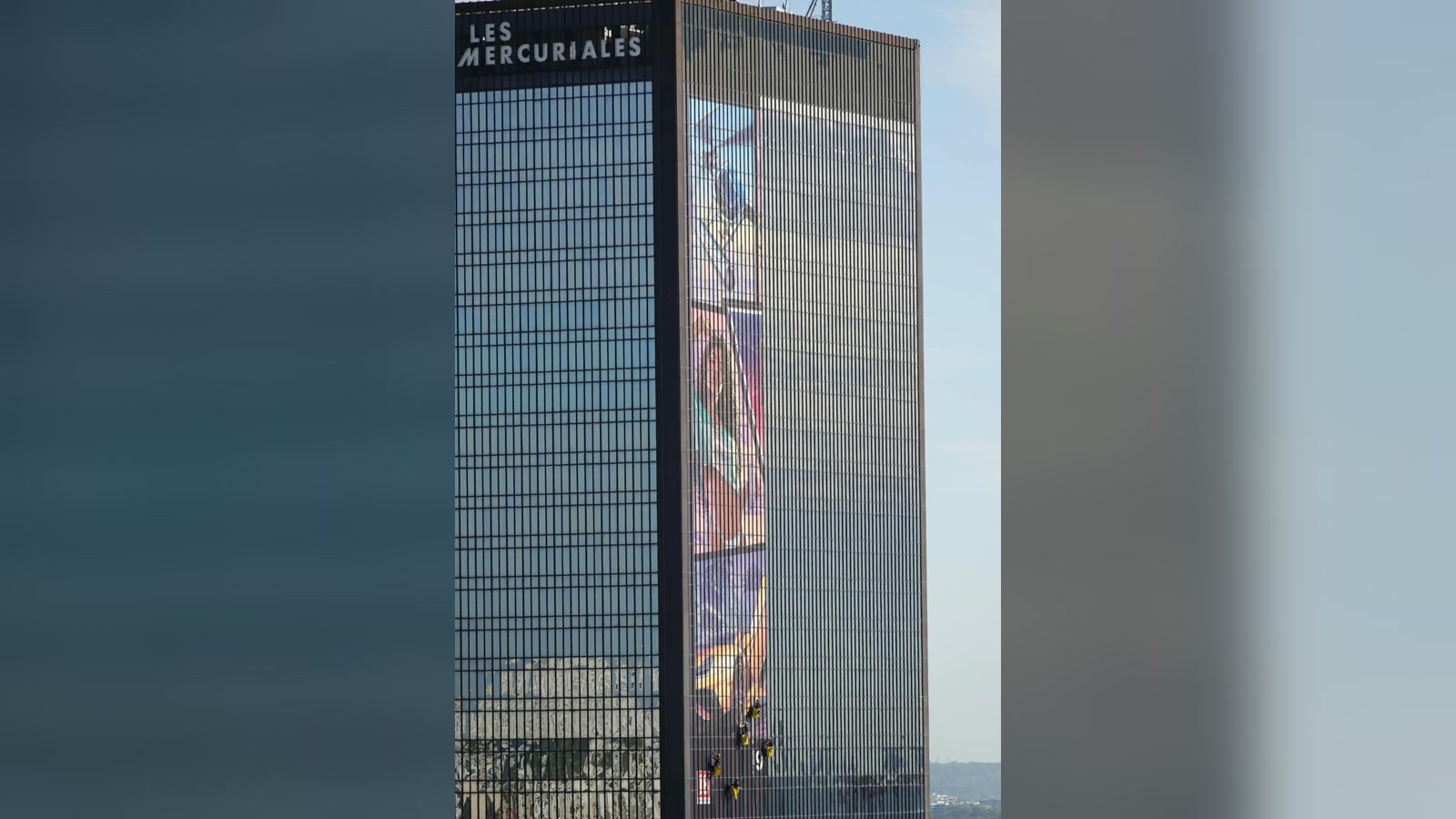 Une tour des Mercuriales, à la porte de Bagnolet, avec une bande d’affiche aux couleurs de GTA VI en cours de pose sur sa façade