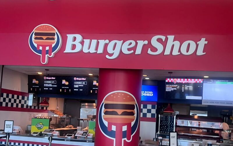 Comptoir de restauration du Kaseya Center de Miami habillé aux couleurs de Burger Shot, avec le logo du burger dégoulinant et un pilier marqué du VI de GTA VI