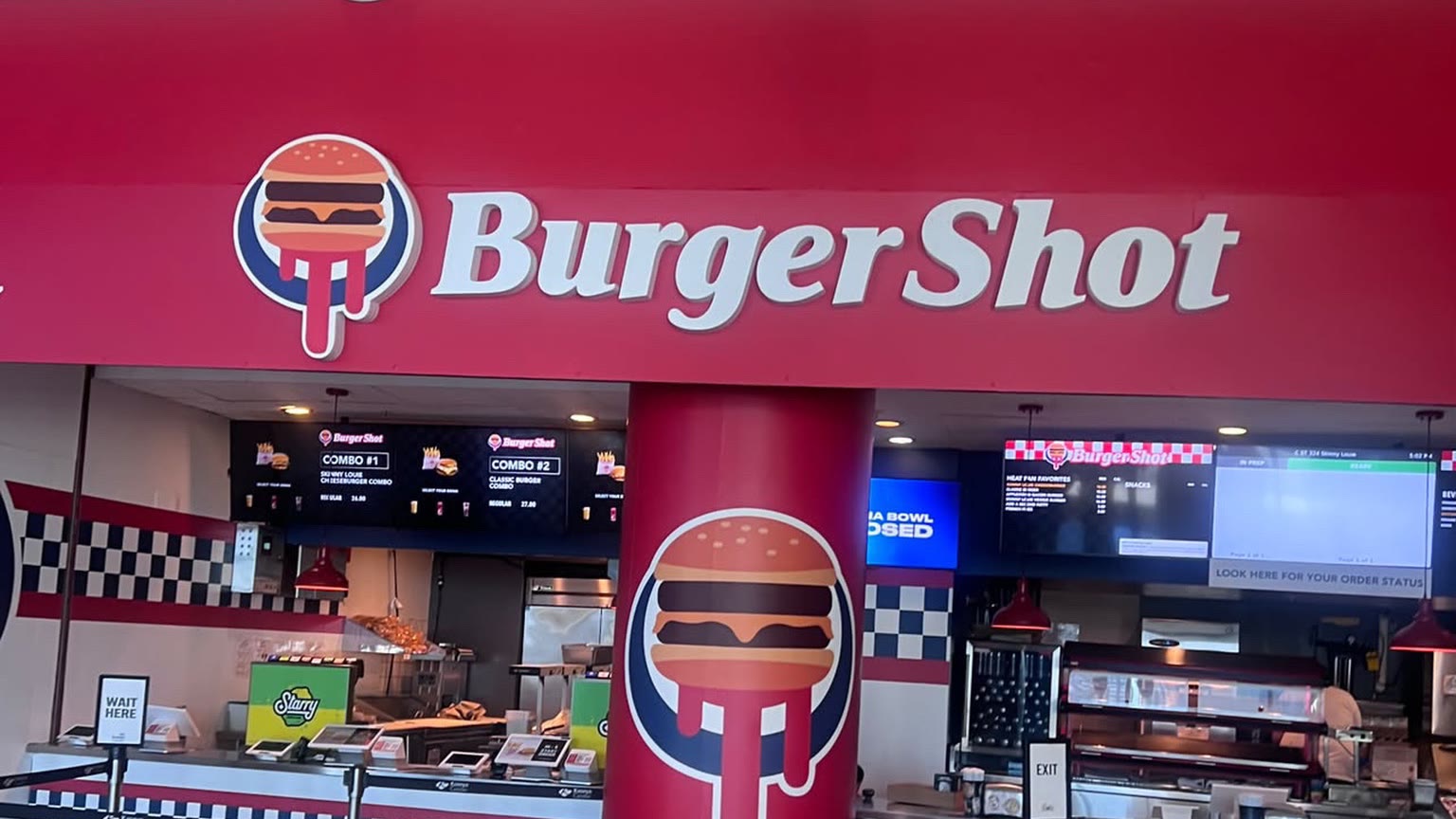 Comptoir de restauration du Kaseya Center de Miami habillé aux couleurs de Burger Shot, avec le logo du burger dégoulinant et un pilier marqué du VI de GTA VI