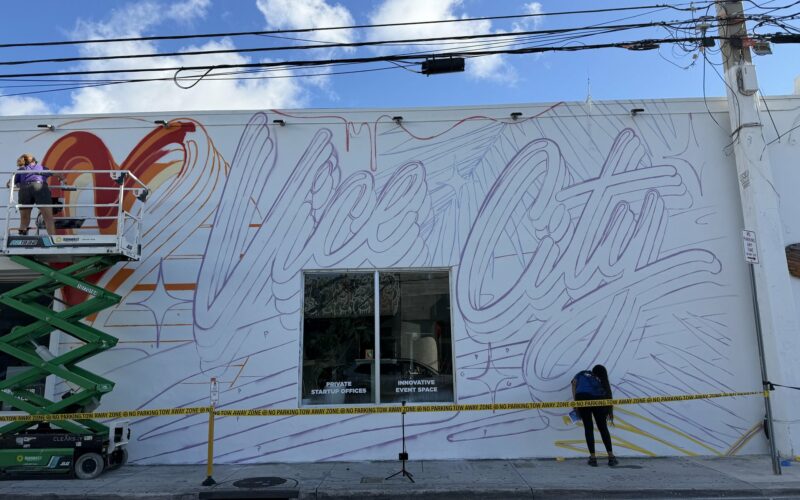 Fresque murale « Vice City » avec un cœur rouge en cours de peinture sur un mur blanc de Wynwood, à Miami, avec une nacelle et une peintre
