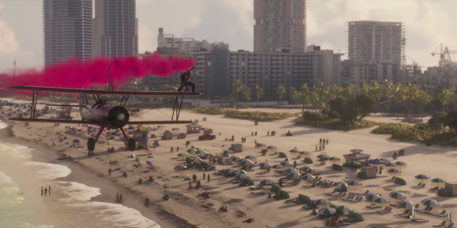 Un biplan rouge laisse une traînée de fumée rose au-dessus d'une plage bondée de Vice City, Launch Trailer de GTA VI