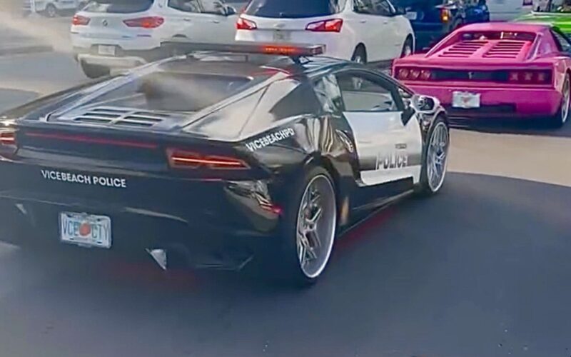 Une Lamborghini noire et blanche aux couleurs de la Vice Beach Police, plaque VCE CTY, roule dans le centre de Miami suivie d’une voiture rose