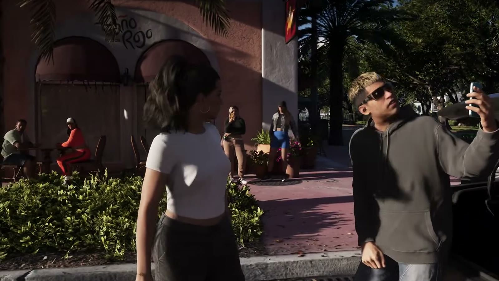 Camilo se filme au téléphone à côté de Lucia dans une rue de Vice City