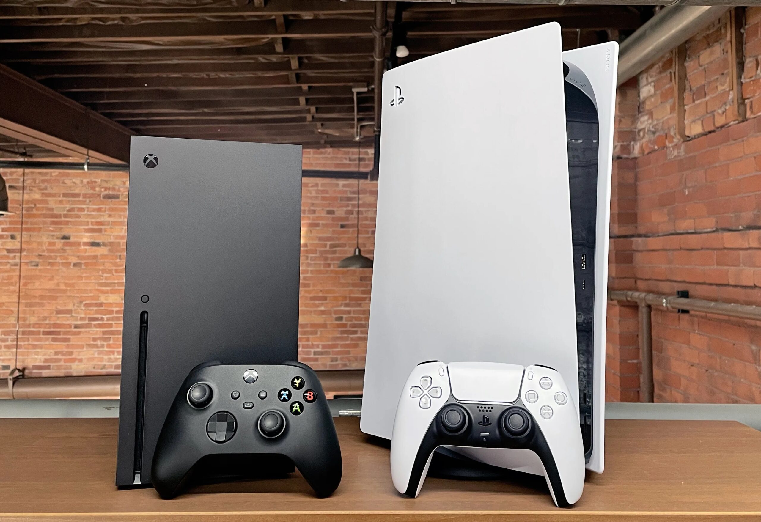 Une Xbox Series X noire et une PlayStation 5 blanche posées côte à côte avec leurs manettes